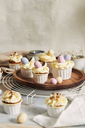 A vertical shot of small cupcakes with white cream and candies on a round wooden board