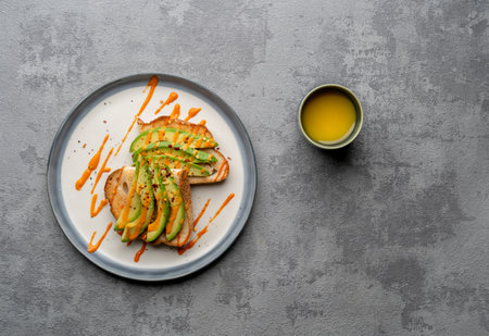 A top view of a delicious avocado toast covered in spicy sauce on a white plate, on a  grey surfaceの写真素材