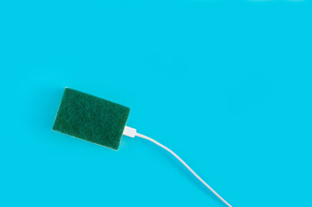 A top view of a USB cable plugged in a kitchen sponge isolated on a pastel blue background