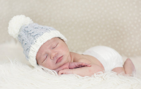 An adorable newborn Caucasian baby boy in bonnet sleeping on a white fur cloth