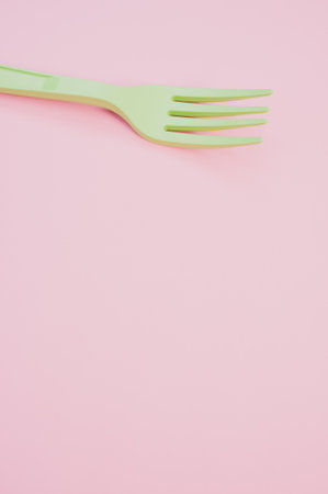 A vertical shot of a plastic fork on a light pink background