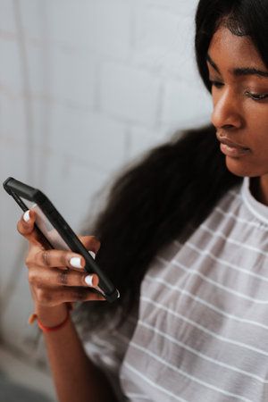 A beautiful young African female using her smartphone in bedの写真素材