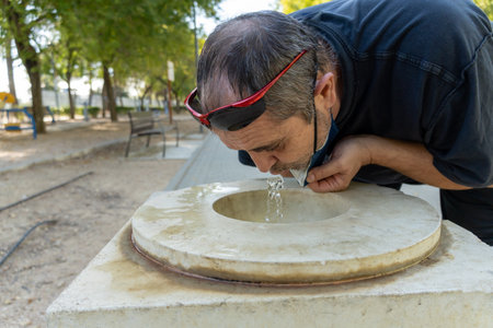 Stock photo of middle age man with face mask drinking water from a fountain.の写真素材