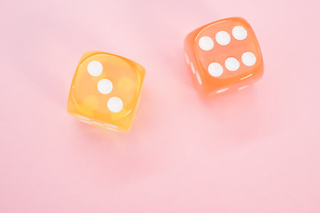 Two orange and yellow dices isolated on pink background