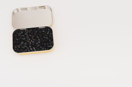 A high angle shot of small black liquorice candies in a metal box isolated on a white backgrou
