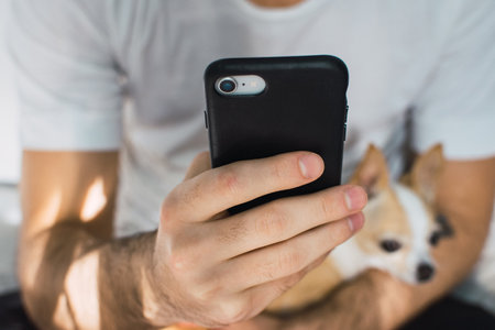 A closeup of a smartphone with a black case in the hands of a dude holding his dog