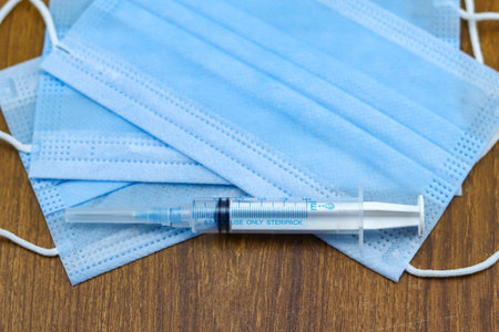 A syringe on face masks on a wooden background - Covid-19 pandemicの写真素材