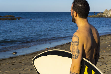 A closeup shot of a Caucasian young male surfer standing on the beachの写真素材