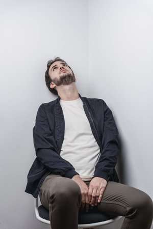 A vertical shot of a Caucasian man staring at the ceiling while seated on a chair at a corner of a...