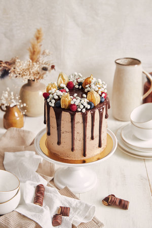 A high angle shot of a delicious chocolate and berry cake on a cake stand in a kitchen with pottery and candies around itの写真素材