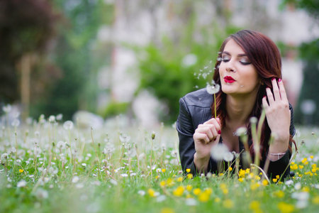 A shallow focus of a young stylish woman lying in a park and blowing a dandelionの写真素材