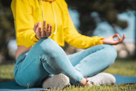 A shallow focus of a person wearing jeans and a yellow hoodie and meditating in a parkの写真素材