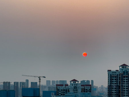 A stunning view of an orange full moon over the rooftops of the bluish city during sunset