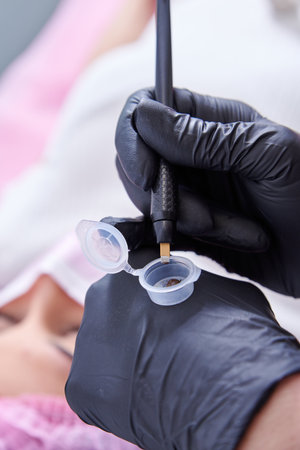 A beauty salon worker hands dipping the tool into the ink during microblading processの写真素材