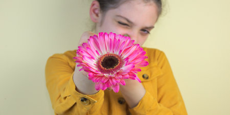 A cute caucasian girl keeping pink chrysanthemum towards the cameraの写真素材