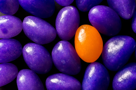 An orange jelly bean standing out among purple beans - concept of standing out from the crowdの写真素材