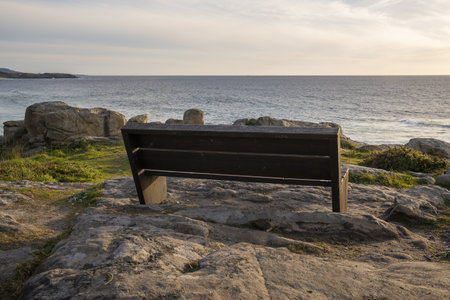 A wooden bench on rocky beach at sunsetの写真素材