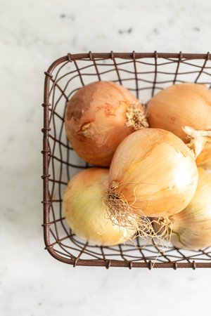 A top view of fresh white onions in a metal basket on a tableの写真素材