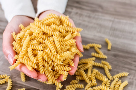 A closeup of a hand holding macaroni on a wooden tableの写真素材