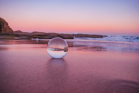 A mesmerizing view of a clear crystal ball placed on the sand near the beach during the sunsetの写真素材
