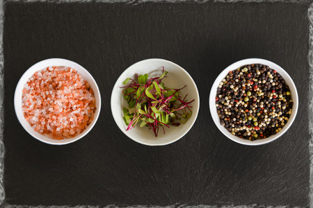 three white bowls on slate background pink salt micro herbs and rainbow pepperの写真素材