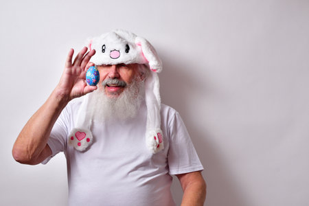 An old man dressed as an Easter bunny holding a decorated egg