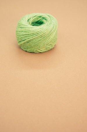 A vertical shot of green macrame cord isolated on peach-colored background