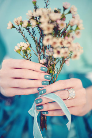 A vertical closeup shot of female hands with blue nail polish holding a bouquetの写真素材