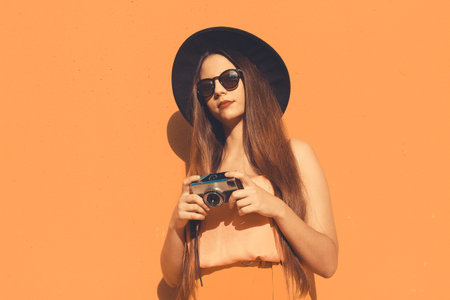 A Spainish woman with a vintage photo camera and wearing sunglasses isolated on an orange backgroundの写真素材