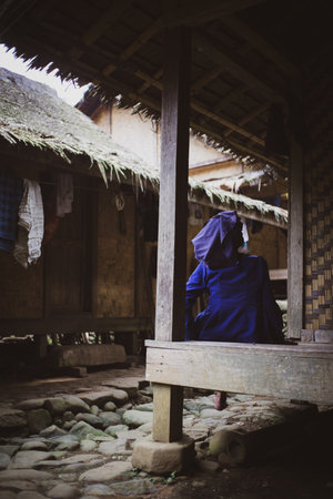 A vertical shot of a female sitting outdoors in a traditional Indonesian houseの写真素材