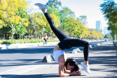 Slender brunette woman doing yoga and the city in the background. handstand with leg stretches