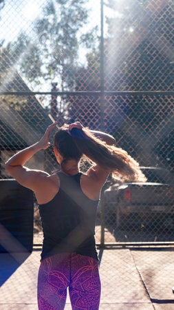 young woman focused on fitness, fixing her hair, to be comfortable while exercising outdoors on a court. Vertical Shot.の写真素材