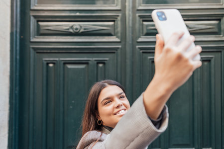 A Caucasian female taking a selfie with her smartphone in a green door background and smilingの写真素材