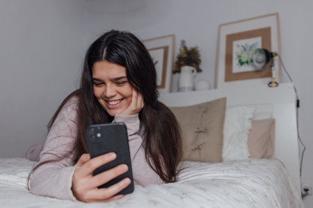 A beautiful Caucasian female using her smartphone while lying on the bedの写真素材