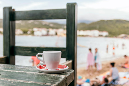 A closeup shot of a cup of coffee on a wooden table at the beachの写真素材