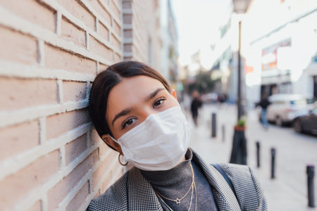 A shallow focus shot of a beautiful Caucasian female with a protective mask leaning on the wallの写真素材