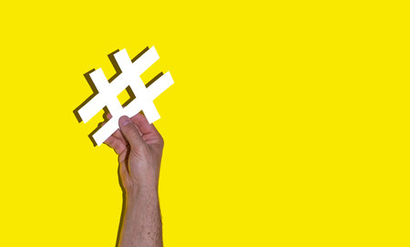 A man's hand holding a white hash on a yellow background - social media day conceptの写真素材