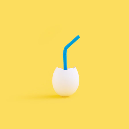 A closeup of a blue plastic straw in an eggshell against the yellow backgroundの写真素材