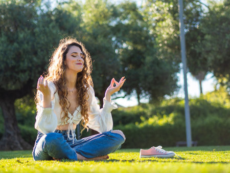 A young Spanish female is meditating sitting on the grass in the spring sunny parkの写真素材