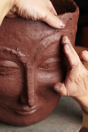 A closeup shot of hands sculpting a clay vase with a faceの写真素材