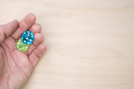 A top view of a hand holding green and blue dice isolated on a wooden surface for a copy space