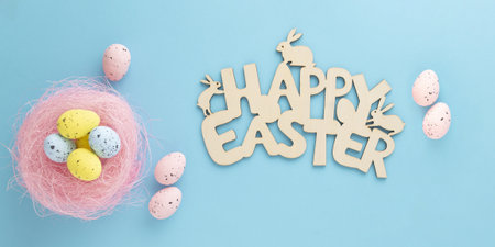 An easter composition made with paschal eggs and a "Happy Easter" wooden sign on blue backgroundの写真素材
