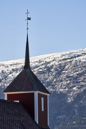 A vertical shot of the Veikaker church surrounded by hills covered in the snow in Norwayの写真素材