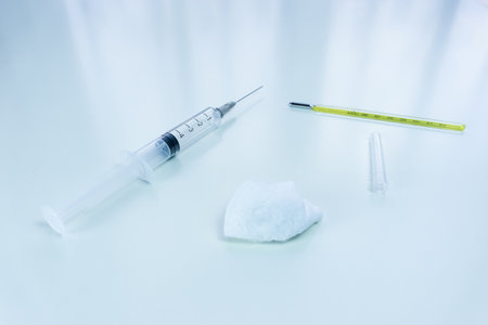 A closeup shot of a thermometer a syringe, and a cotton ball at a hospitalの写真素材
