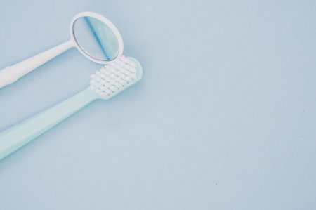 A top view of a blue toothbrush next to a dental mouth mirror on pastel blue surface for a copy spaceの写真素材