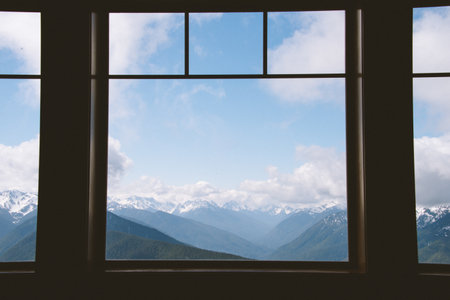 A mesmerizing view of the snowy mountains under the cloudy blue sky from the window