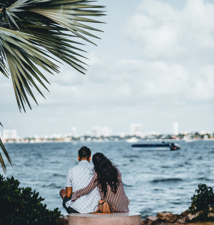 A selective focus shot of a loving couple from behind hugging each other and looking at the sea