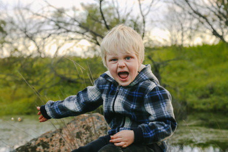 A cute little blonde kid sitting on a rock in a parkの写真素材