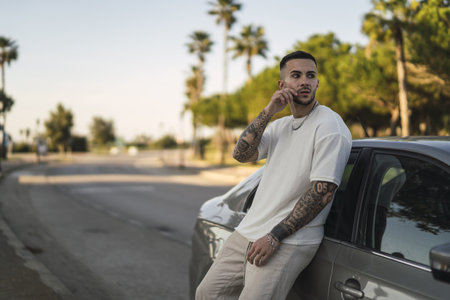 A young tattoed European man leaning on his carの写真素材