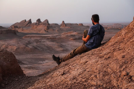 A Young man contemplating the horizon in the desert of Lut (Dasht-e-Lut) and its characteristic rock formations or Kalutsの写真素材